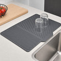 Dark grey kitchen drying mat with drainage ridges beside a sink